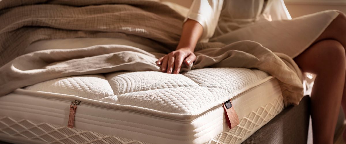 Frau sitzt auf einer hochwertigen Matratze mit weicher Steppung und einer beigen Decke – Fokus auf Komfort und Gemütlichkeit. Frau sitzt auf einer hochwertigen Matratze mit weicher Steppung und einer beigen Decke – Fokus auf Komfort und Gemütlichkeit.