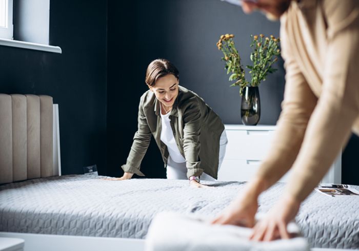 Zwei Personen machen ein Bett in einem modernen Schlafzimmer mit Blumen im Hintergrund Zwei Personen machen ein Bett in einem modernen Schlafzimmer mit Blumen im Hintergrund
