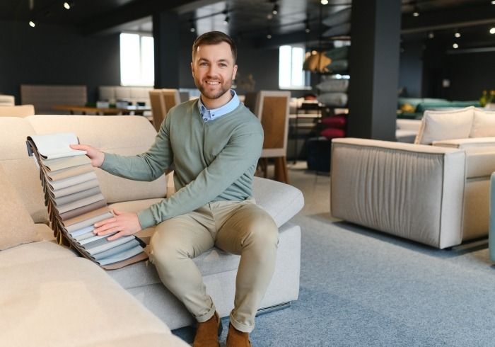 Ein Mann sitzt auf einem Sofa in einem Möbelgeschäft und zeigt eine Auswahl an Stoffmustern für Polstermöbel.