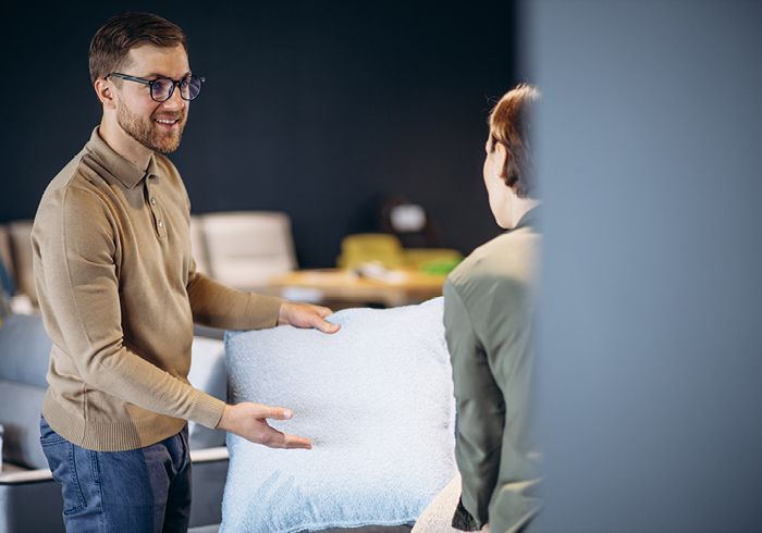 Mann zeigt einer Frau ein Kissen in einem modernen Einrichtungsgeschäft – Fokus auf Beratung und Komfort